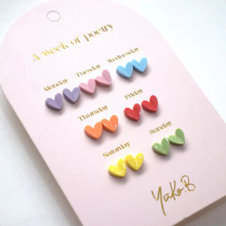 Zeven paar hartjesoorbellen in paars, roze, blauw, oranje, rood, geel en groen op een roze kaart met Engelse weekdagen.
