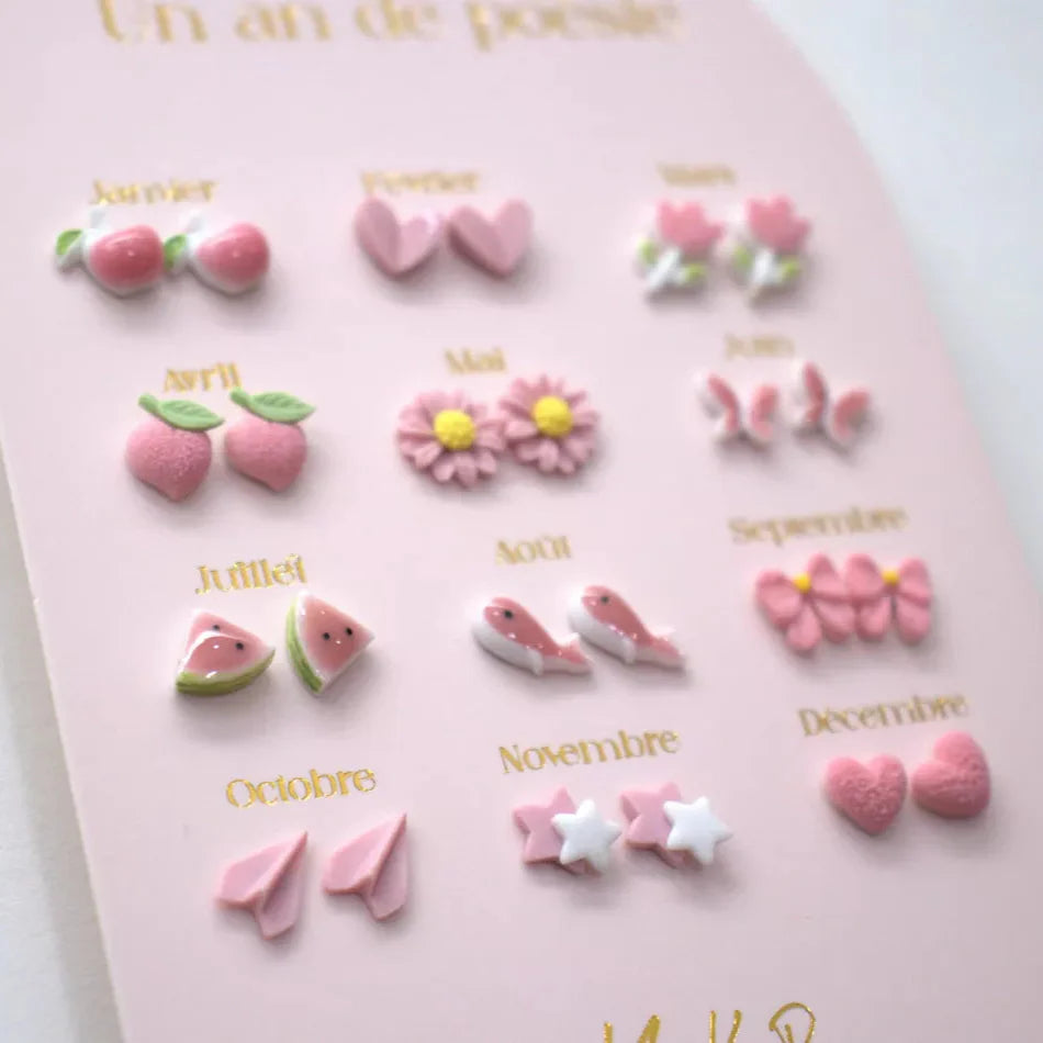 Roze kaart met twaalf paar oorbellen in vormen zoals vlinders, watermeloenpartjes, vogels en papieren vliegtuigjes.