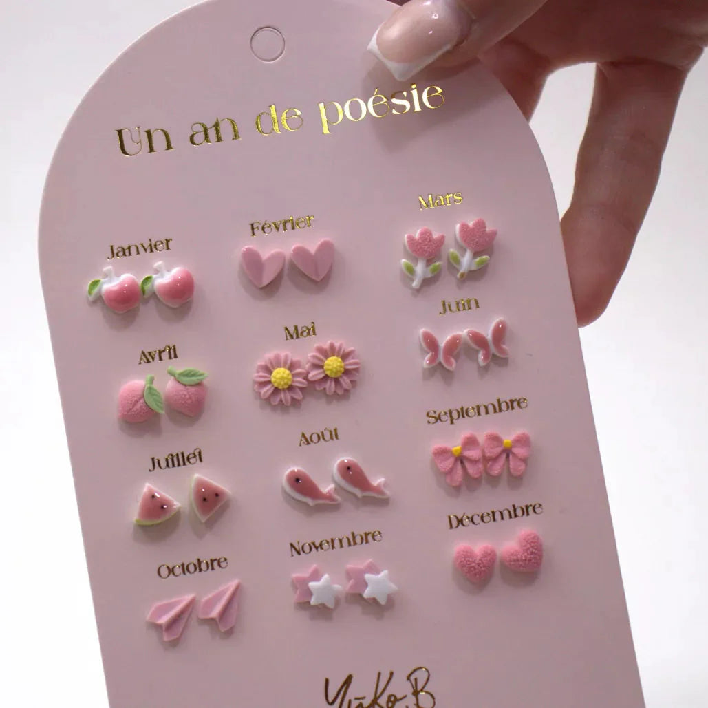 Een hand houdt een roze kaart vast met twaalf paar oorbellen in roze thema, gerangschikt per maand.