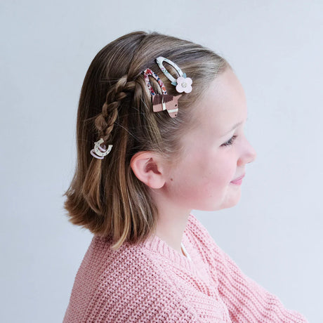 Meisje in zijaanzicht met paarden- en bloemenhaarclips naast een vlecht en een roze vest.