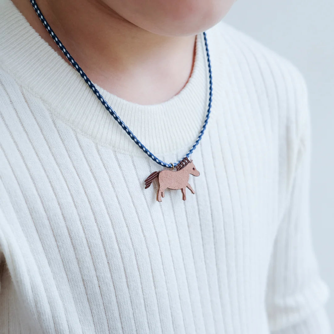 Detail van een blauw-witte ketting met bruin paardje, gedragen op een witte geribde trui.