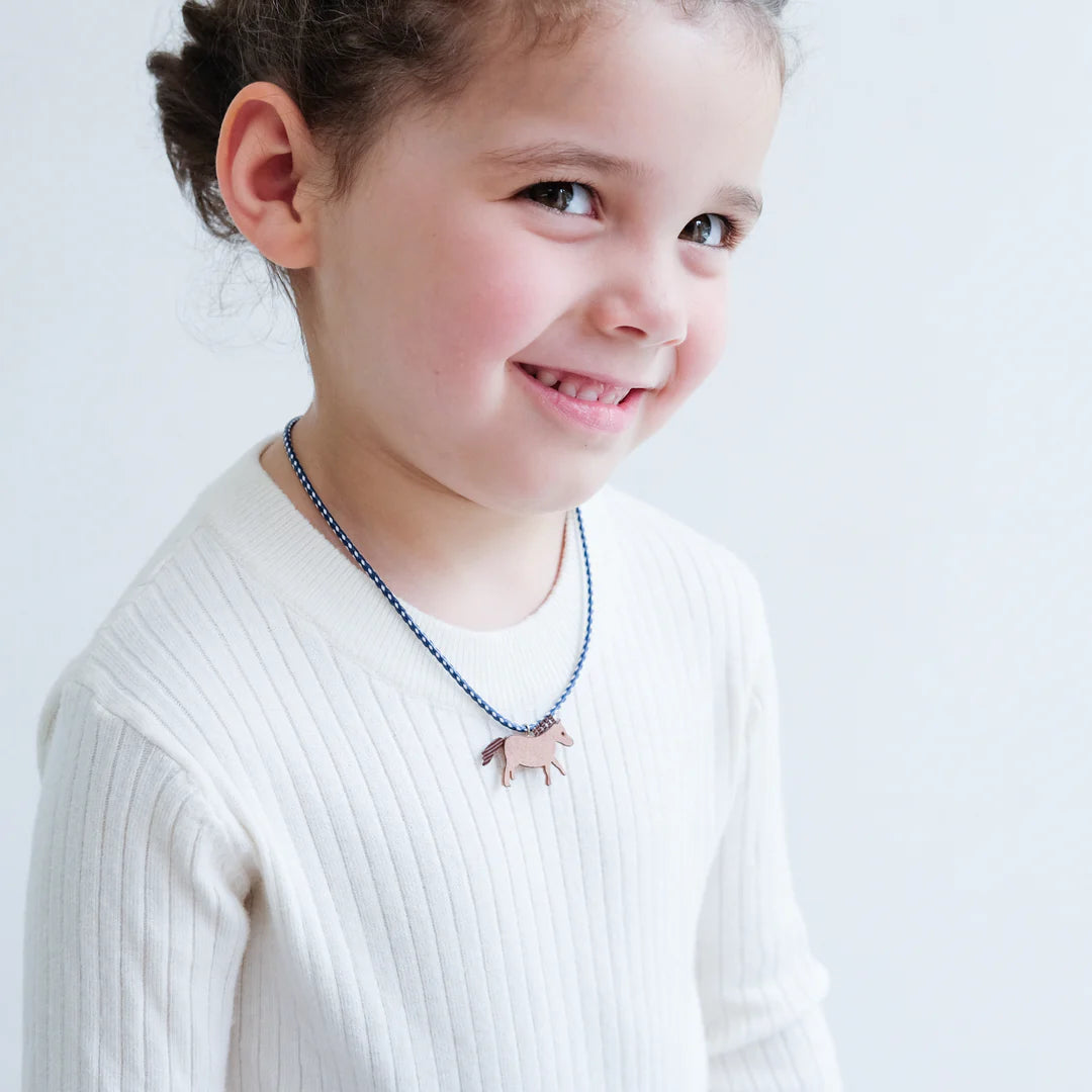 Kind in een witte trui draagt een blauw-witte ketting met een bruin paardje.