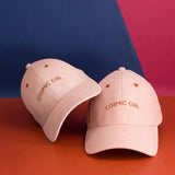 Twee roze corduroy petten Cosmic Girl met karamelkleurig borduursel op een oranje ondergrond.
