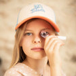 Kind draagt de Let's Dance-pet met ecru voorkant, koraalkleurige klep en lichtblauw borduursel.