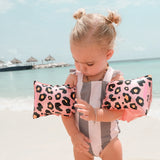 Kind met rosékleurige zwembandjes met panterprint en een gestreept badpak op het strand.