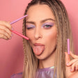 Model met paarse oogmake-up houdt een paars en roze Skyliner-oogpotlood vast tegen een roze achtergrond.