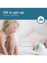 Kind zit rechtop in bed naast roze slaaptrainer Sam met open ogen en een groene wijzerplaat.