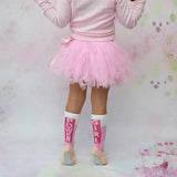 Kind met roze Girl Power-sokken, een roze tutu en balletschoenen, van achteren gezien.