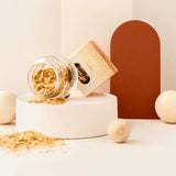 Star Dust Gold gezichtsglitter in een gekanteld glazen potje, met losse gouden glitters en verpakking op een witte sokkel.