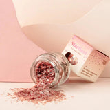 Star Dust Pink Star gezichtsglitter in een gekanteld glazen potje, met uitgestrooide roze glitter en verpakking erachter