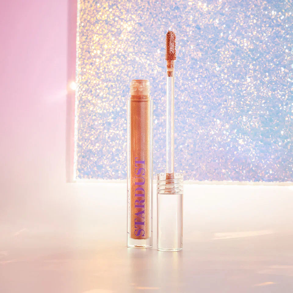Stardust Topper Camille in een transparant flesje met applicator en koperkleurige glans, tegen een glinsterende achtergrond.