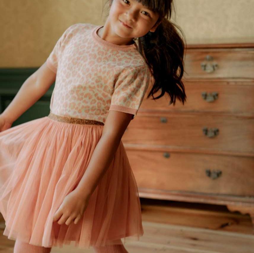 Meisje draagt de roze tule rok Dawn Pink met een shirt met luipaardprint voor een houten ladekast.