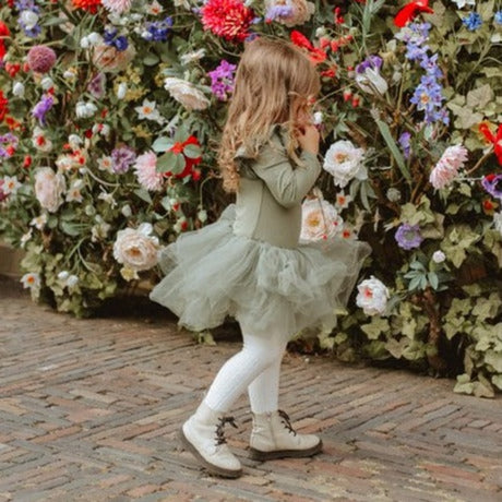 Meisje in een mosgroene balletjurk met tuturok, witte panty en lichte laarsjes voor een bloemenwand.