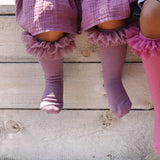 Detail van paarse tutu kniekousen met ruches aan de benen van een zittend kind, naast een felroze kous.