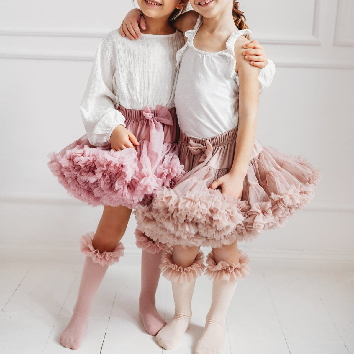 Twee kinderen naast elkaar in tutu rokken met roze en lichtgekleurde kniekousen met ruches.