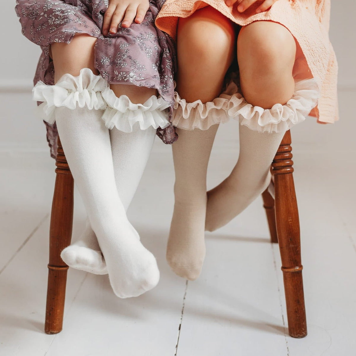 Detail van twee kinderen op een houten stoel met tutu kniekousen met ruches onder hun jurken.
