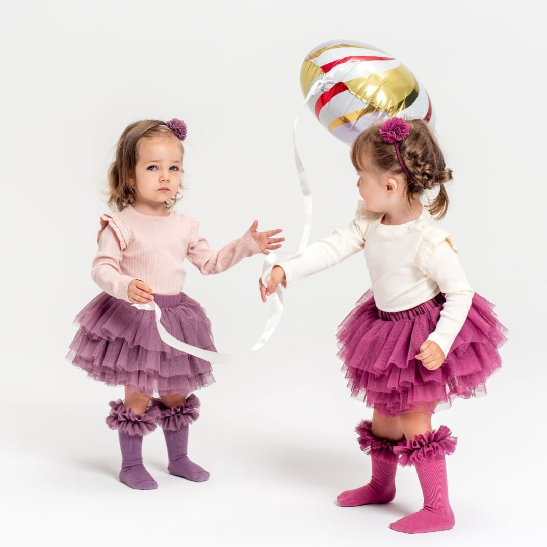 Twee kinderen met tutu kniekousen met ruches in paars en roze, bijpassende rokjes en een ballon.