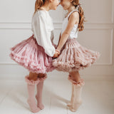 Twee kinderen houden elkaars handen vast in tutu rokken en roze en lichtroze kniekousen met ruches.