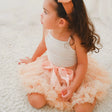 Meisje zit op een licht vloerkleed met de perzikkleurige Loli tutu rok met strik en ruches.