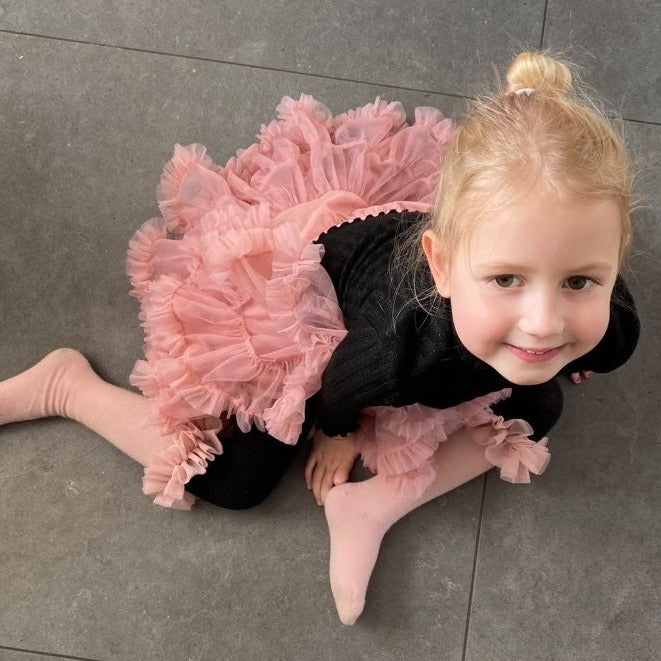 Meisje zit op een grijze tegelvloer in een roze Loli tutu rok, gecombineerd met een zwarte top.