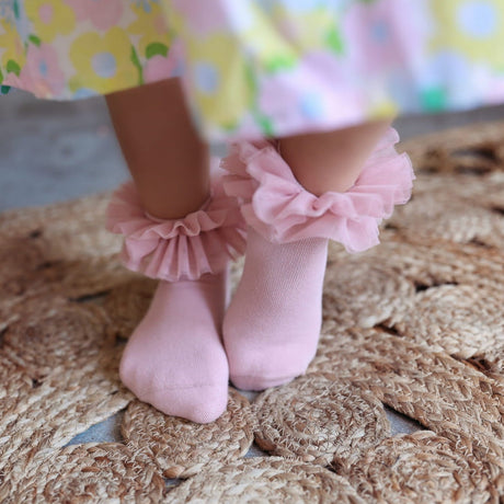 Oudroze tutu sokken met ruches, gedragen onder een gebloemde jurk op een gevlochten kleed.
