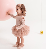 Kind met roze tutu-sokken en een bijpassende rok en haarband, naast een grote roze ballon.
