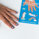 Hand met blauwe nagelstickers met eenhoorns, een regenboog en een zon naast de verpakking.