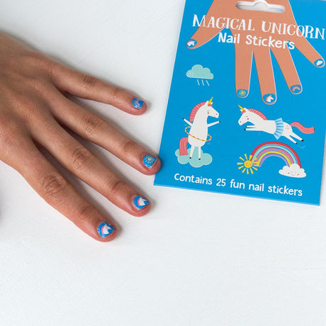 Hand met blauwe nagelstickers met eenhoorns, een regenboog en een zon naast de verpakking.