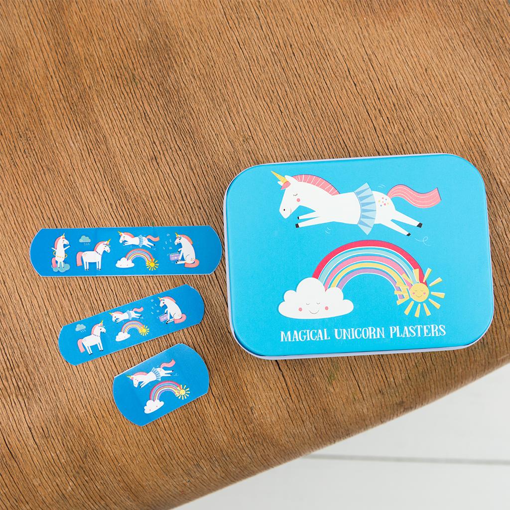 Blauw eenhoornblik met daarnaast drie blauwe pleisters met eenhoorns en regenbogen op een houten tafel.