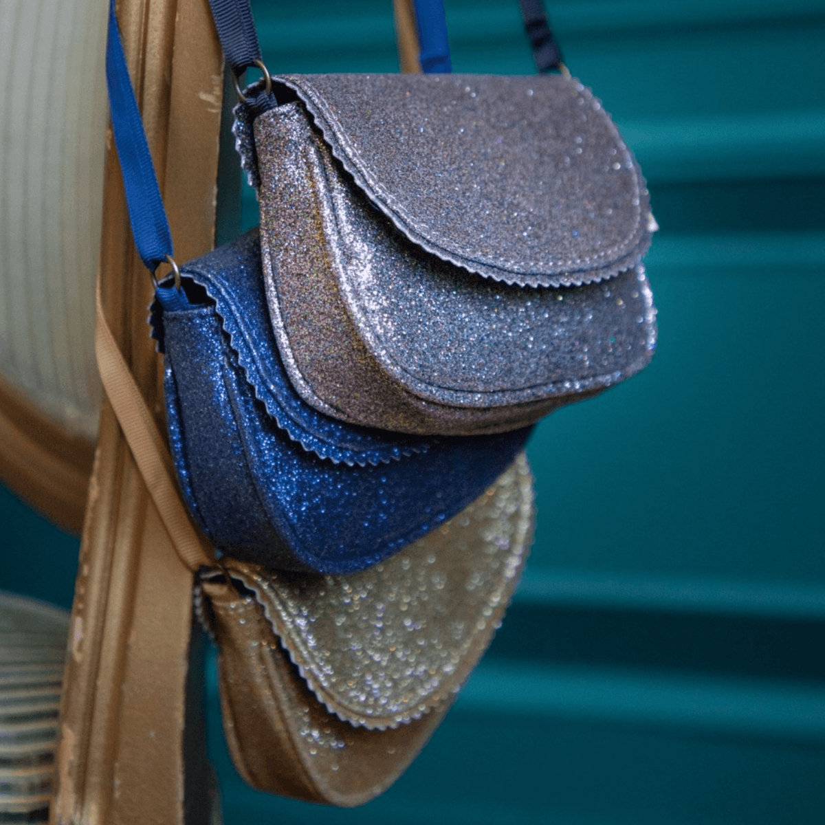 Lavendelkleurige Urfa schoudertas met glitters, hangend boven een blauwe en goudkleurige glittertas.
