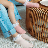 Licht abrikooskleurige en roze sokken met witte kanten ruches, gedragen bij jeans naast een rotan tafel.
