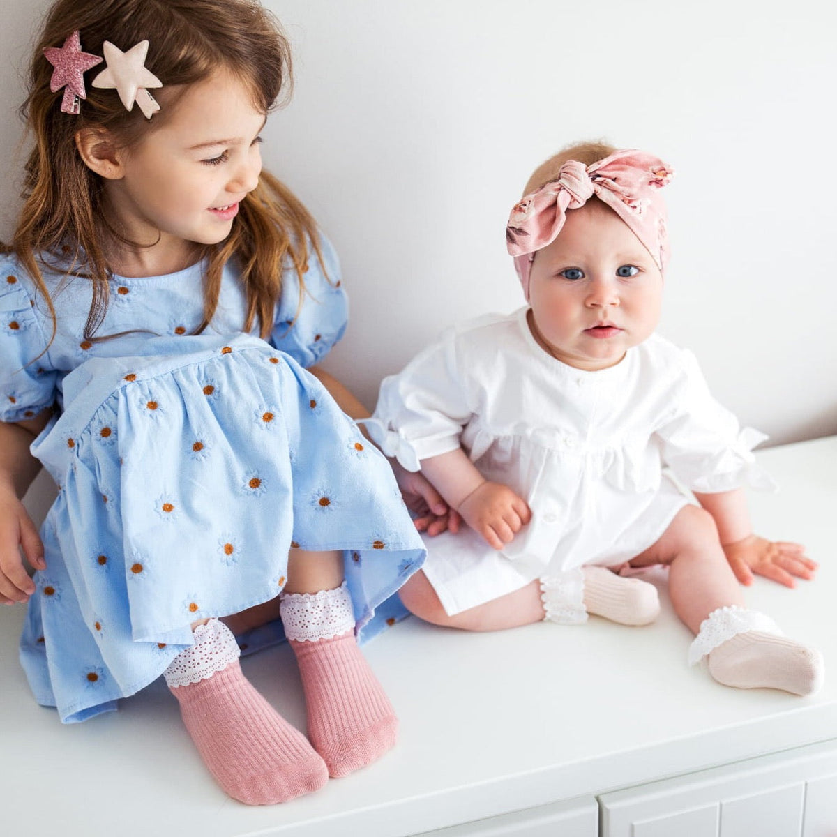 Meisje met oudroze Vintage Love-kousen met wit kant naast een baby met crèmekleurige kousen.