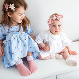 Meisje met oudroze Vintage Love-kousen met wit kant naast een baby met crèmekleurige kousen.