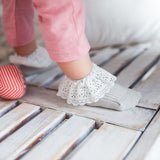 Kind met roze broek en grijze Vintage Love sokken met witte kanten boord op een houten ondergrond.