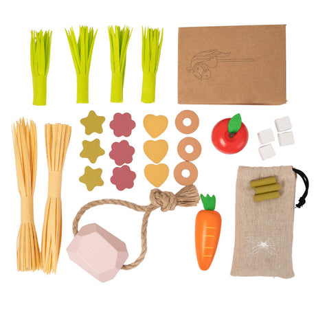 Voederset voor een stokpaard, uitgestald met appel, wortel, stro, groene stengels, snoepjes, voerzakje en roze liksteen.