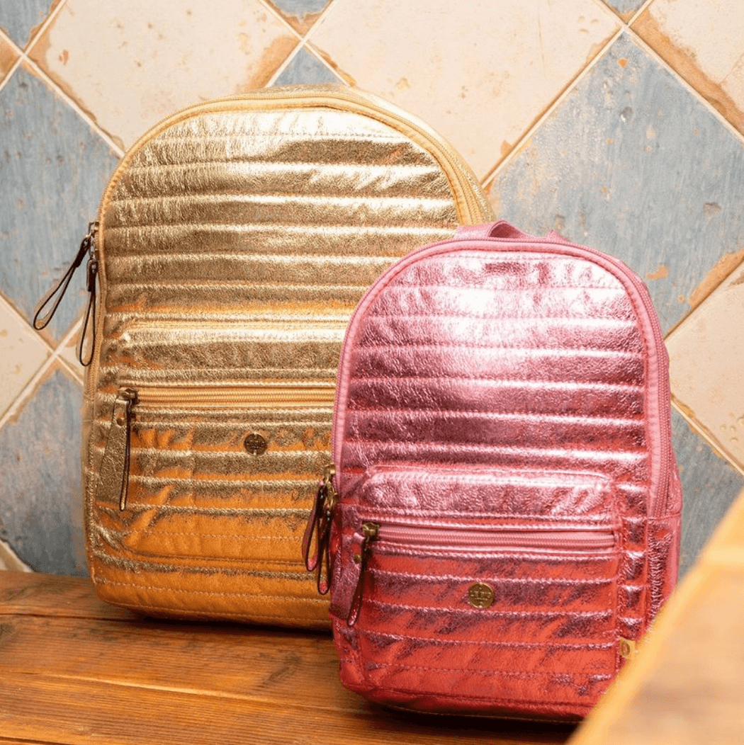 Glanzend roze Walker rugtas met voorvak, naast een groter goudkleurig exemplaar op een houten tafel.