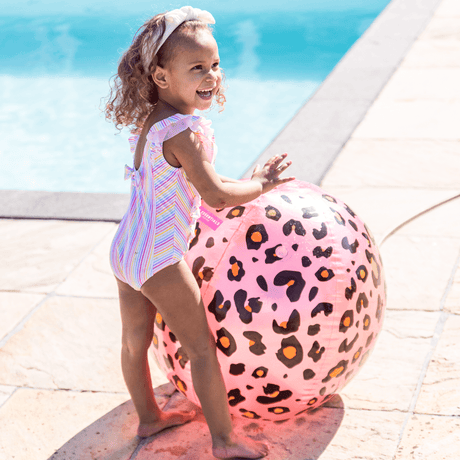 Kind met een hand op de roze, bolvormige watersproeier met panterprint naast het zwembad.