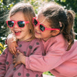 Twee kinderen met een roze Aspen zonnebril Camellia Rose omhelzen elkaar buiten.
