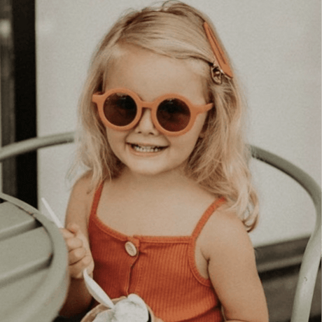 Kind met de Kidooz Apricot zonnebril op, zittend aan tafel met een ijsje.