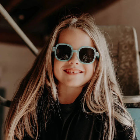 Kind met lang blond haar draagt de mintgroene Koody Percy kinderzonnebril met donkere glazen.