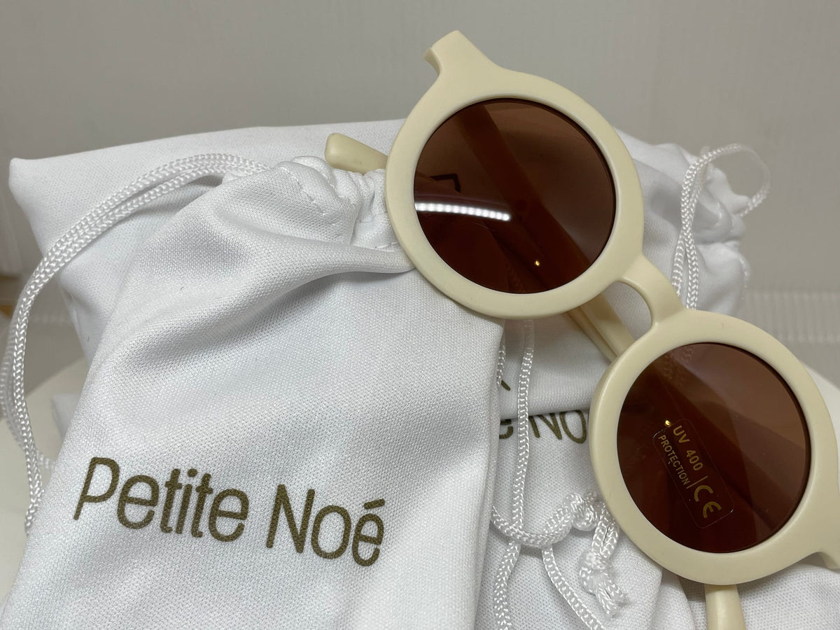 Petite Noé zonnebril in Creamy Milk met bruine glazen op een wit bewaarzakje met Petite Noé-logo