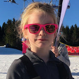Kind draagt de neonroze Koolsun Wave zonnebril in de sneeuw.
